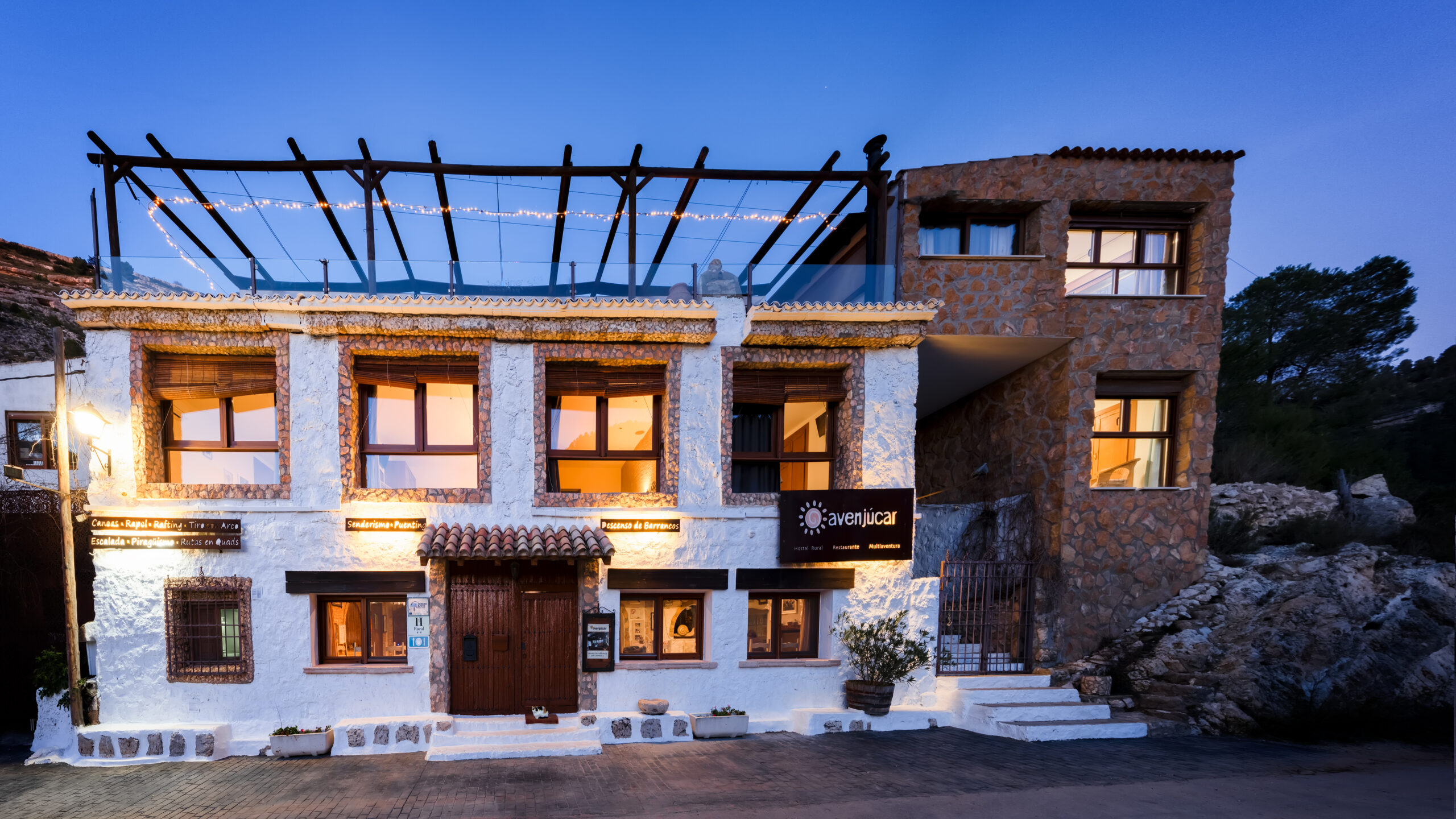 Fachada iluminada de hotel rústico al atardecer.