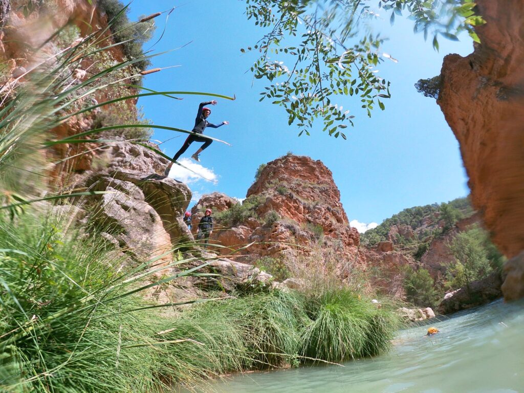 Persona haciendo slackline sobre río en cañón verde.